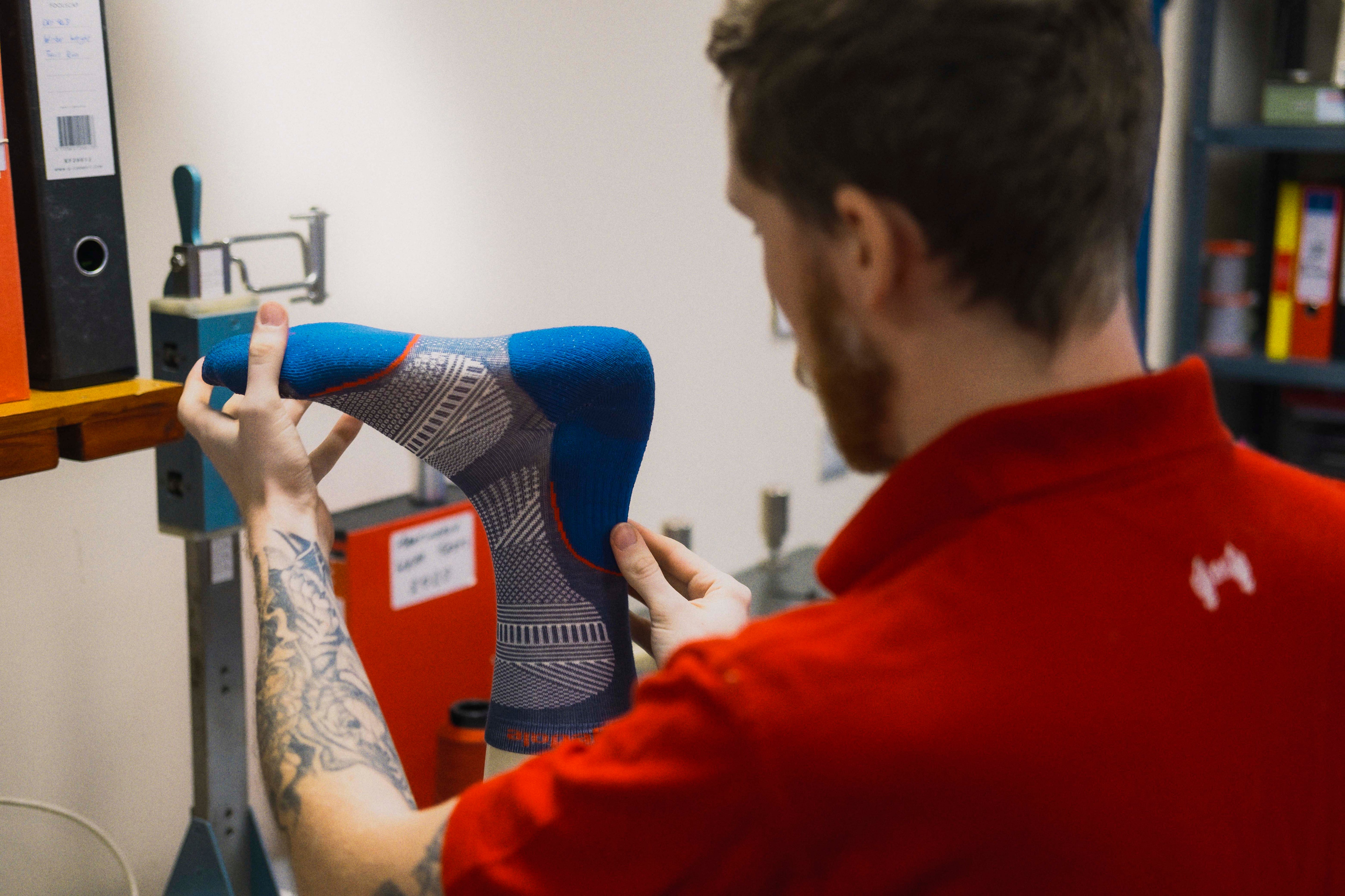 Person wearing a red shirt examining a blue and gray shoe in an indoor setting.