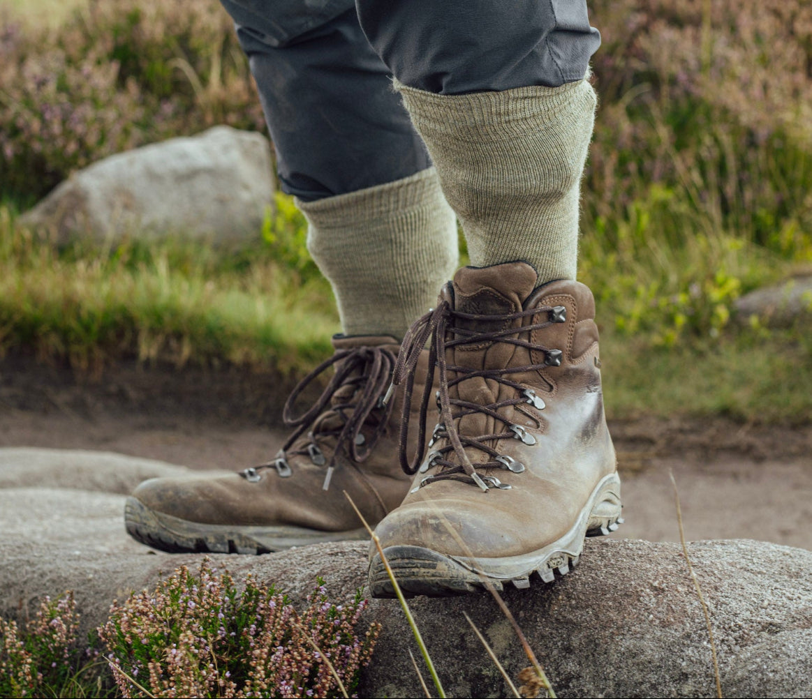 Brown hiking boots on a rock with grass and rocks in the background