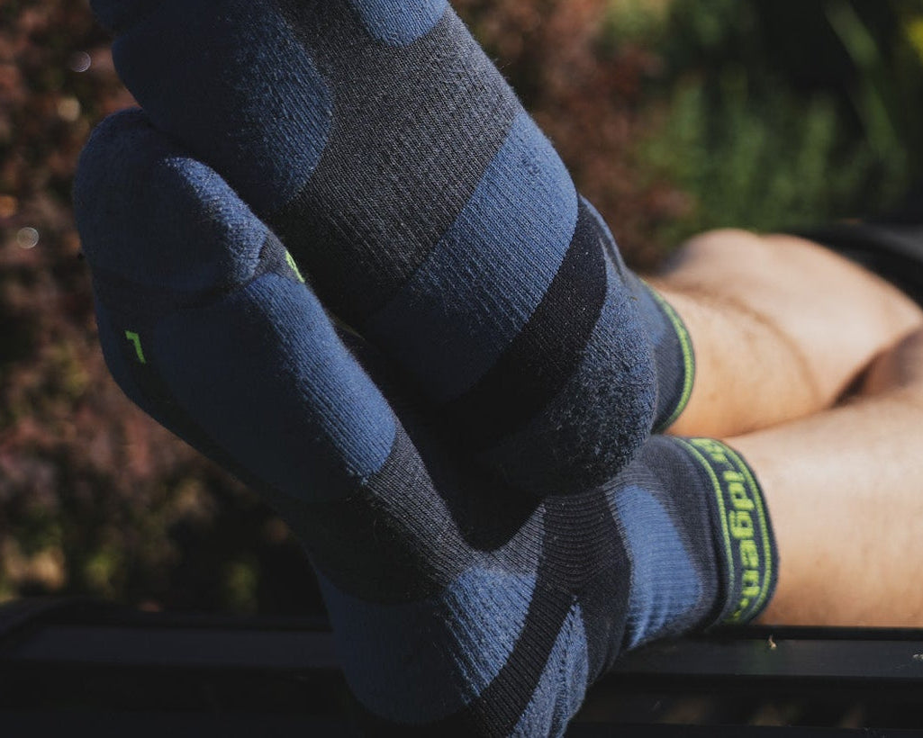 Person lying on a sun lounger with feet up, wearing blue socks and a black shirt, in a garden setting.