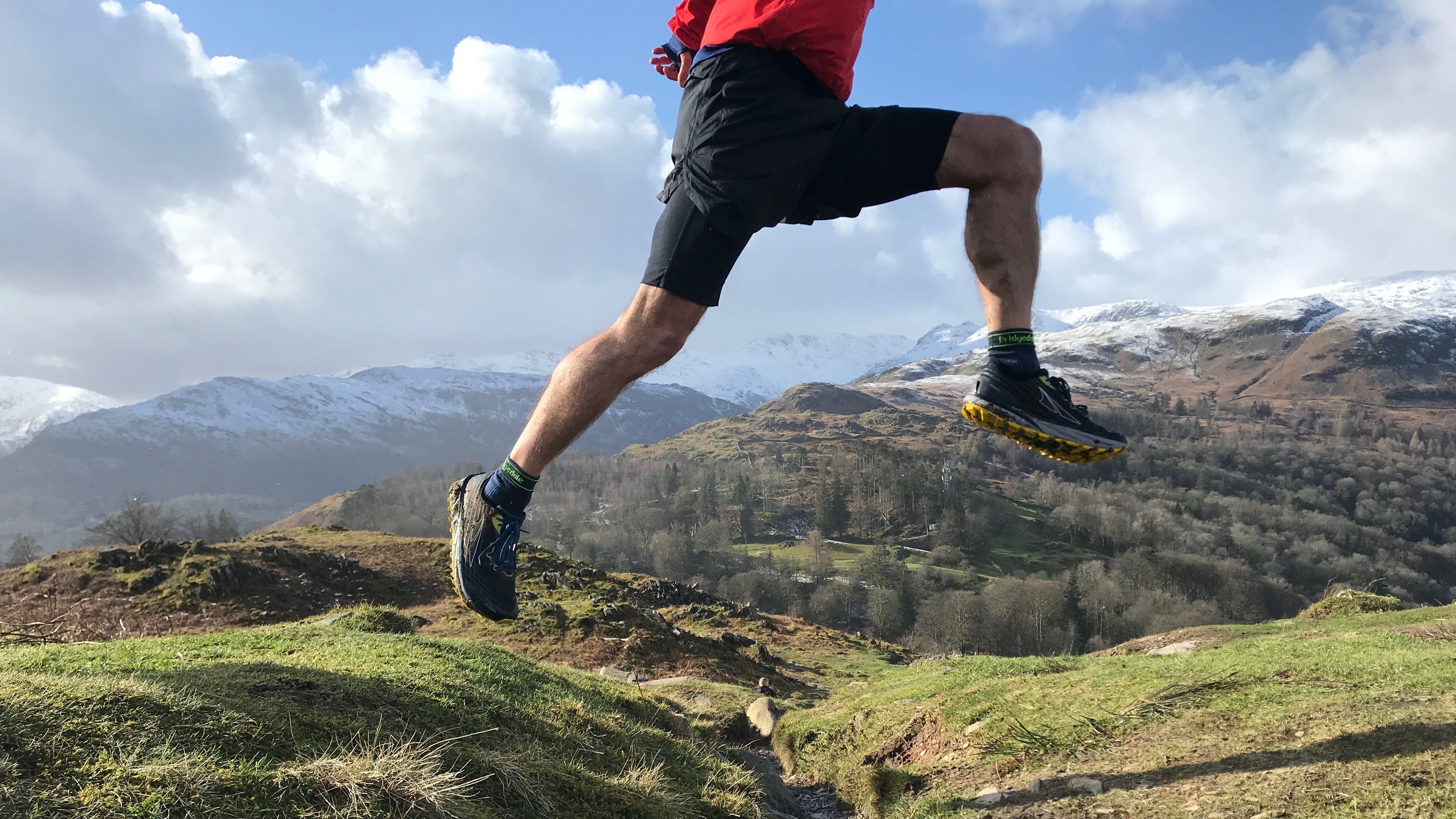Person running on a mountain trail with snow-capped peaks in the background